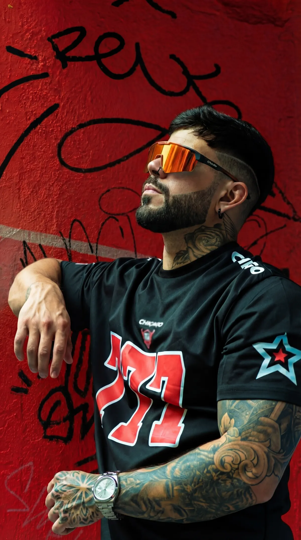 HIDEKI con gafas naranjas y camiseta 777 frente a graffiti rojo